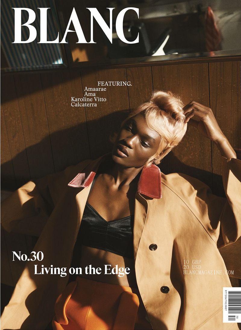 Fashion magazine cover featuring a Black woman with short blonde hair wearing a beige trench coat and black bralette in a studio.