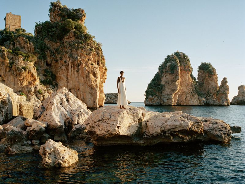 Model Awar Odhiang standing on a rocky outcrop wearing a white dress for Aritzia High Summer 2026 campaign.