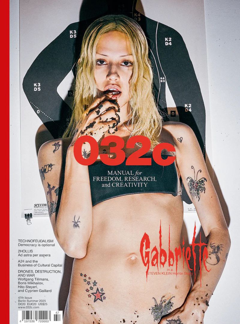 Magazine cover featuring a model with tattoos, holding hands covered in a dark substance, posed in front of a target silhouette.