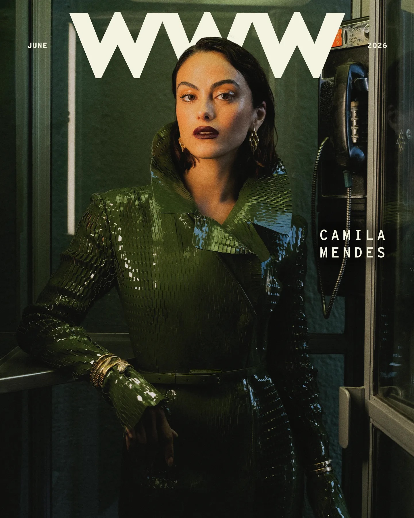 Camila Mendes wearing a glossy dark green patent trench coat inside a vintage telephone booth for Who What Wear magazine.