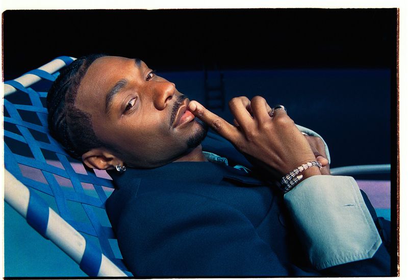 Jonathan Daviss reclining on a blue webbed lawn chair with finger to his lips for Who What Wear.