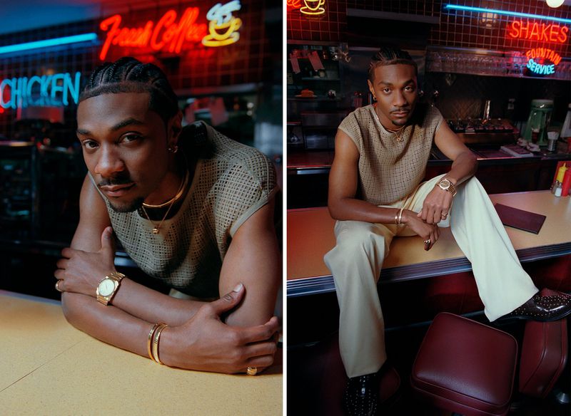 Jonathan Daviss wearing a textured sleeveless knit top and cream trousers posing in a diner with neon signs
