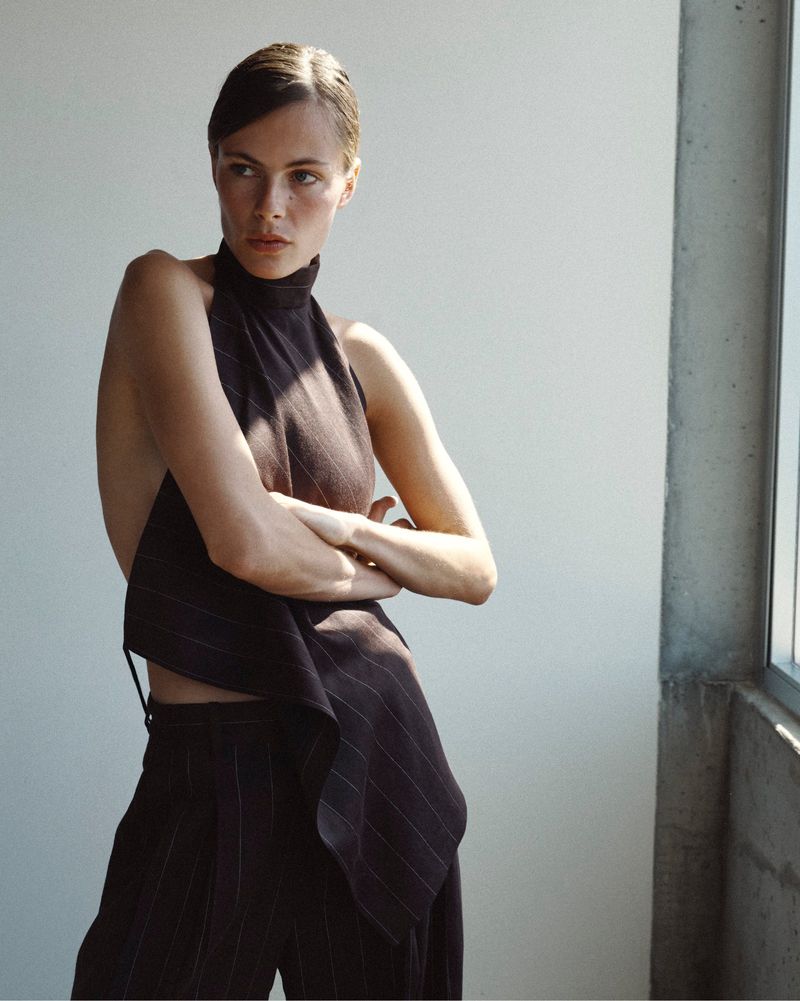 Model with arms crossed wearing an asymmetrical pinstripe halter top and matching trousers in natural light.