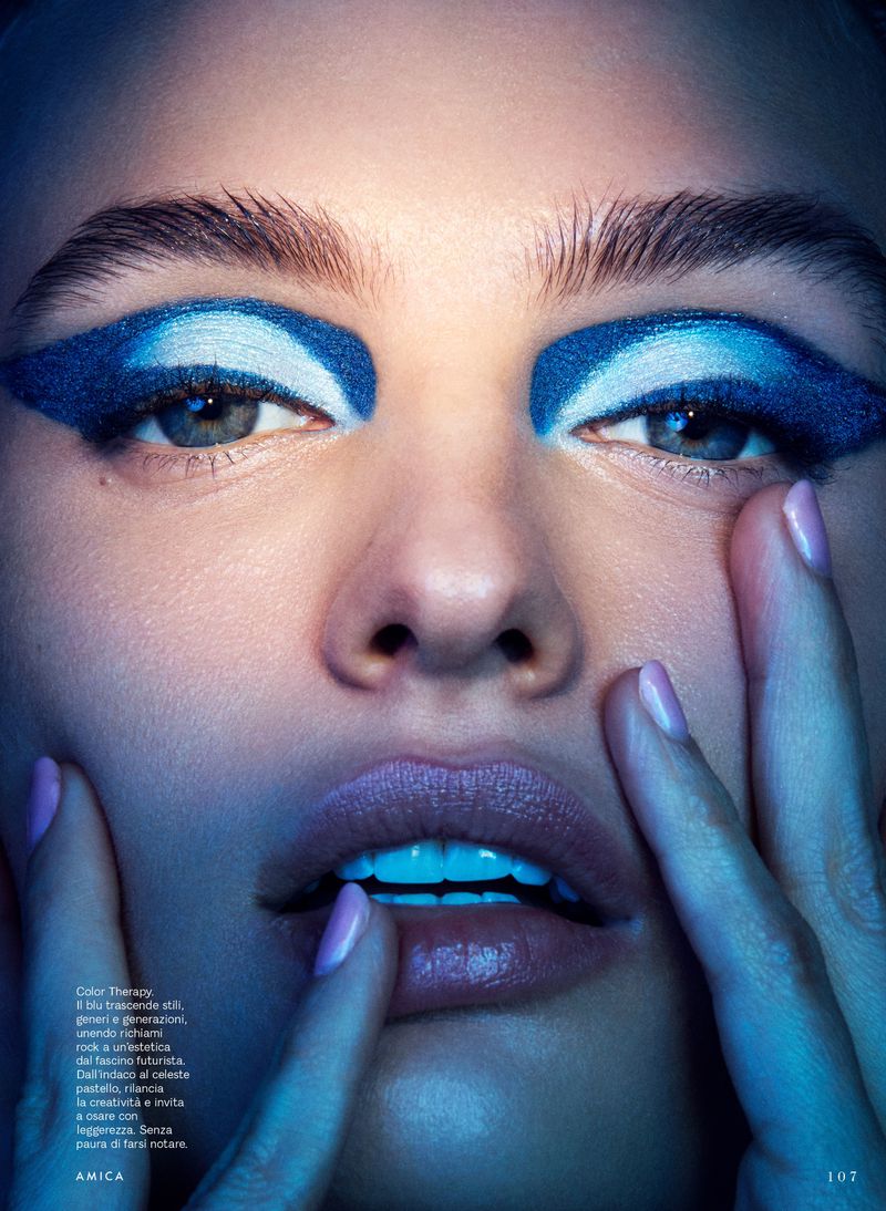 Close-up beauty portrait of Veronika Vilim wearing bold graphic blue eyeshadow and glossy lips with hands touching her face.