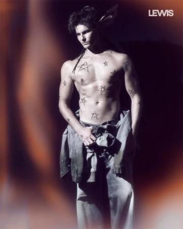 Shirtless male model with star body art wearing denim jeans in high-contrast lighting for Lewis Magazine.
