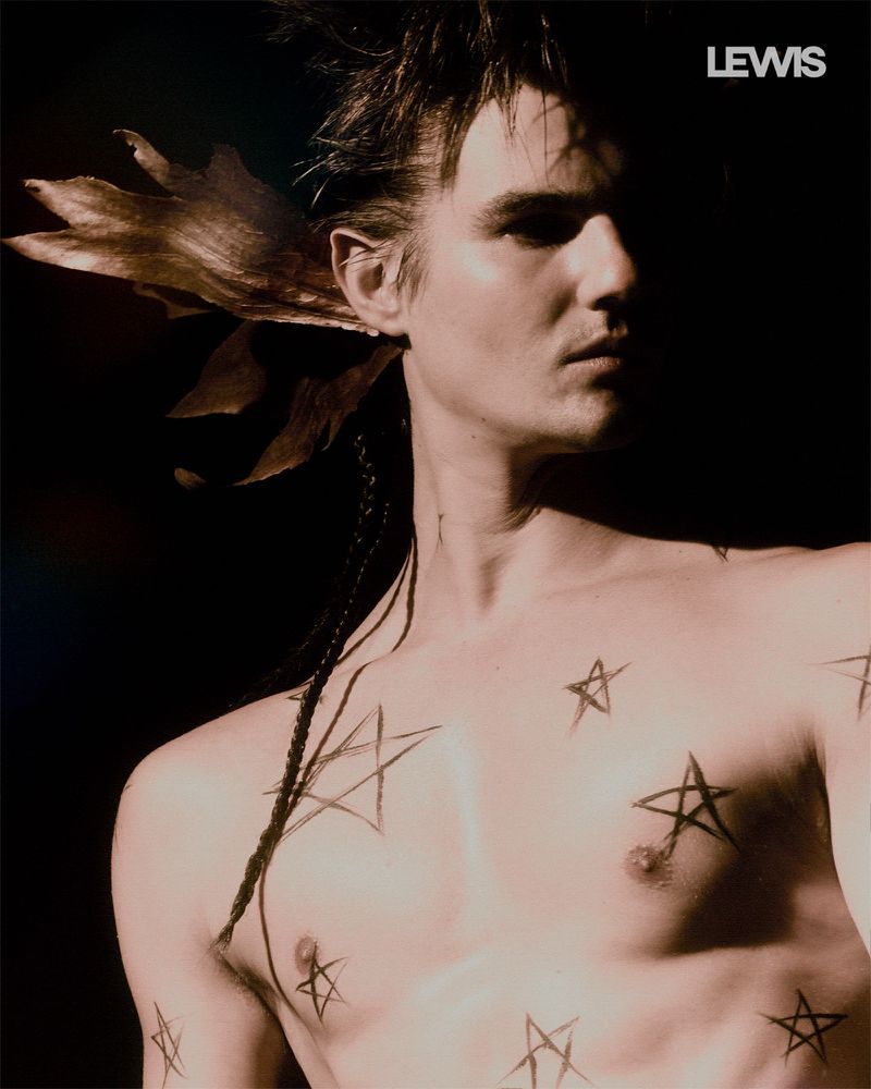 Shirtless man with hand-drawn star markings across his chest and spiky dark hair against a black background.