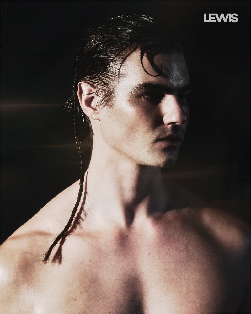 Shirtless man with slicked-back dark hair, a single thin braid, and prosthetic pointed ears in profile against a dark background.