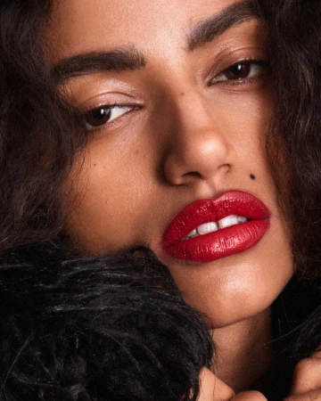 Close up portrait of a woman with glossy red lips and dark curly hair wearing textured black apparel