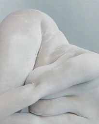 Sculptural close-up of a human body coated in matte white powder against a pale grey background.