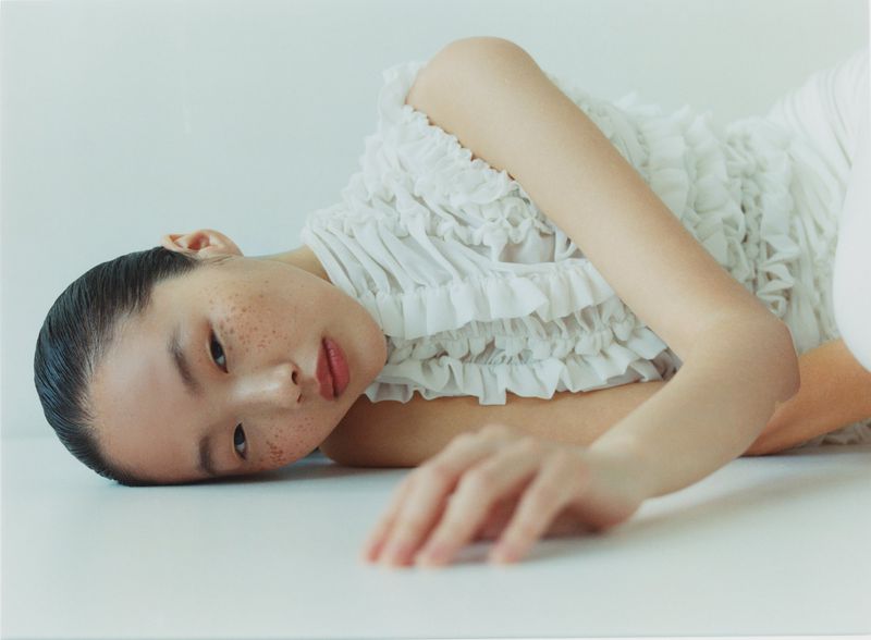 Model lying on white studio floor wearing a white textured ruffled top