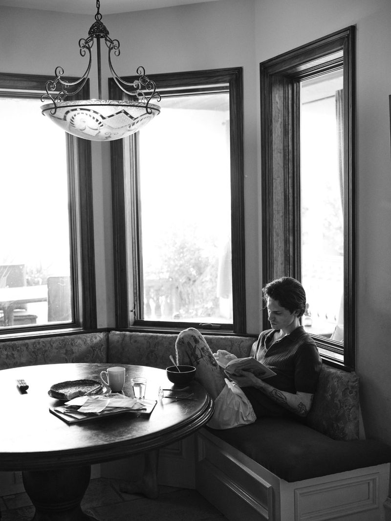 Monochrome image of Justin Eric Martin reading a book on a banquette in a domestic interior by Giampaolo Sgura for Arena Homme +.