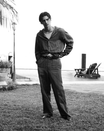 Black and white photo of Justin Eric Martin standing on a grass lawn wearing a hooded shirt and wide-leg trousers.
