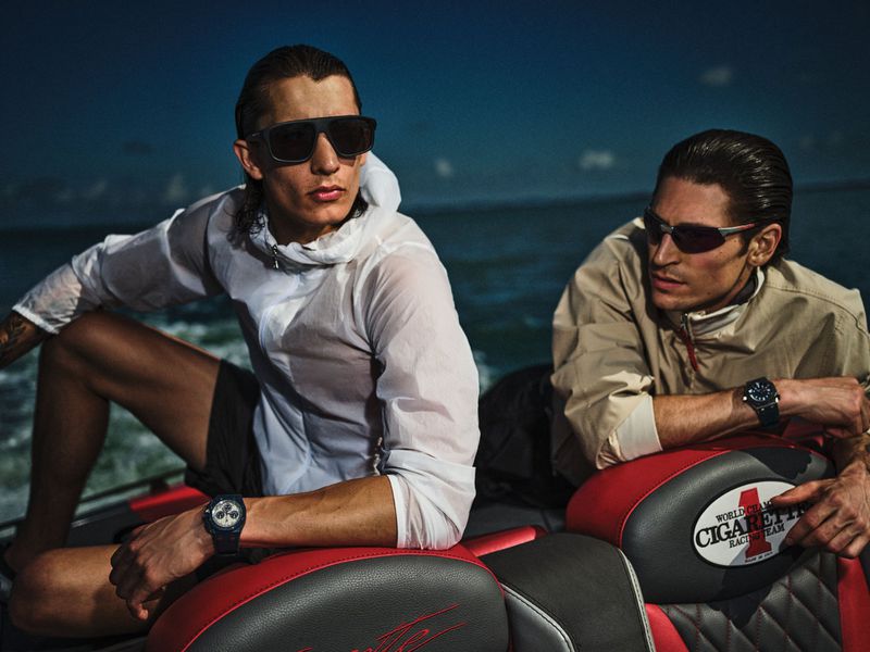 Two male models in sunglasses wearing casual jackets aboard a speeding boat on the ocean for Arena Homme + editorial