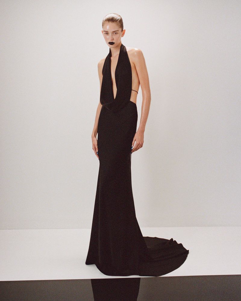 Elegant adult woman in a black halter gown with bare back, standing in a bright photo studio with a black and white checkered floor.