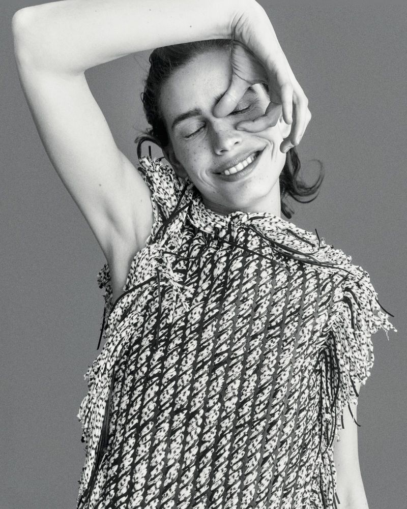 Black and white portrait of smiling model Sean Levy posing with her hand over her eye in a textured fringed sleeveless top.