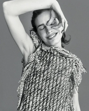 Black and white portrait of smiling model Sean Levy posing with her hand over her eye in a textured fringed sleeveless top.