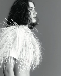 Model Sean Levy in profile wearing an avant-garde white sculptural fringe garment against a neutral studio backdrop.