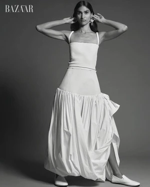 Hannah Wick poses in a white square-neck top, drop-waist gathered maxi skirt, and white flats against a studio backdrop.