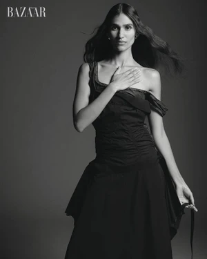 Model Hannah Wick poses in a black off-the-shoulder ruched dress against a dark seamless backdrop.