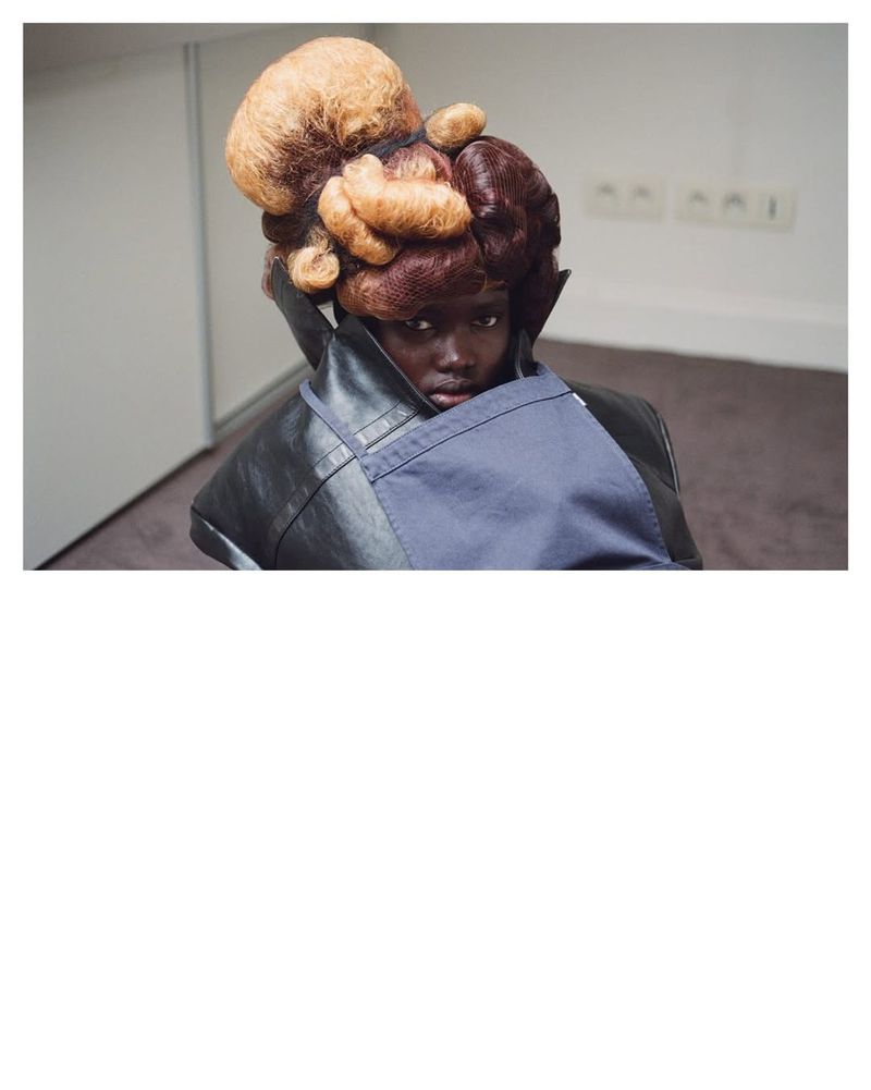 Model Nyakong Chan with a sculptural two-tone hairstyle wearing a high-collar coat and blue drape.