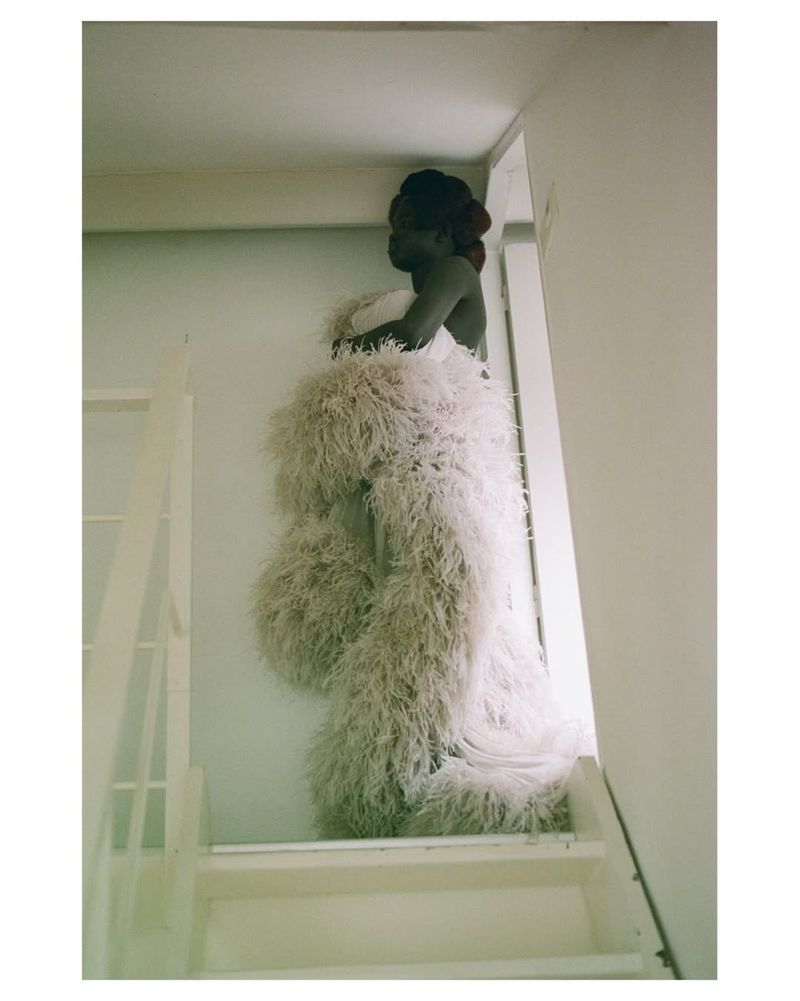 Model Nyakong Chan posing at the top of a white staircase wearing a voluminous off-white feather gown for SSAW Magazine.