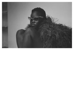 Nyakong Chan wearing futuristic dark sunglasses and a feathery textured collar in a black and white editorial portrait.