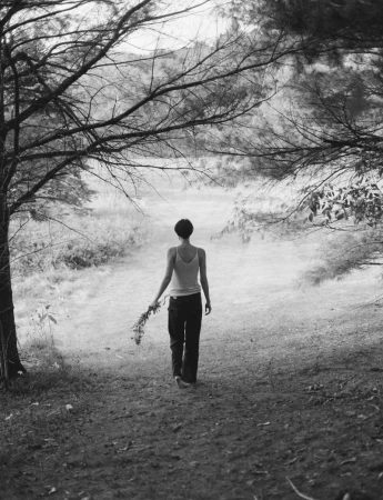 Model Kit Pugh seen from behind walking barefoot through trees wearing a tank top and dark pants for Polène.