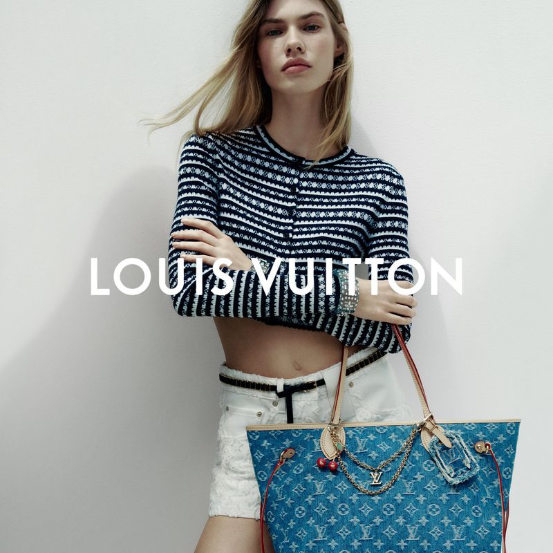 Fashion shot of an adult female model wearing a striped sweater and white shorts, posing with a Louis Vuitton handbag against a white background.