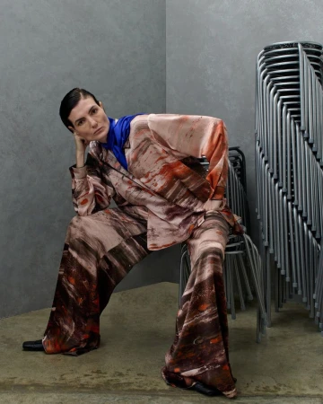 Model Eliana Weirich seated in an earthy brushstroke-printed matching suit and blue scarf for Roksanda Spring/Summer 26.