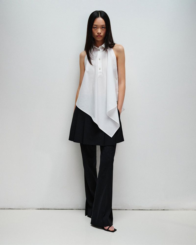 Model Jiayi Liang posing in an asymmetrical white sleeveless collared top and layered black flared pants against a white backdrop.