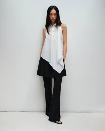 Model Jiayi Liang posing in an asymmetrical white sleeveless collared top and layered black flared pants against a white backdrop.