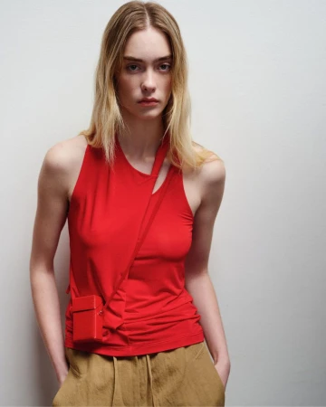 Model in a red asymmetric top wearing brown trousers against a white studio background