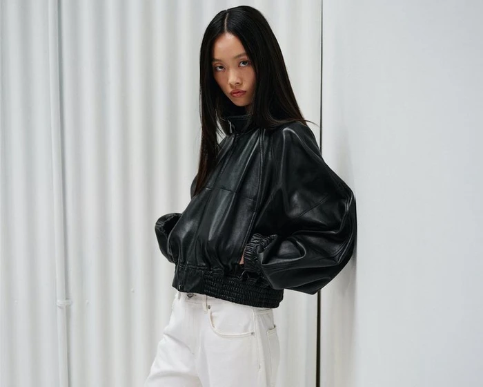 Model Jiayi Liang poses in a voluminous black leather bomber jacket and white jeans against a white backdrop for Helmut Lang.