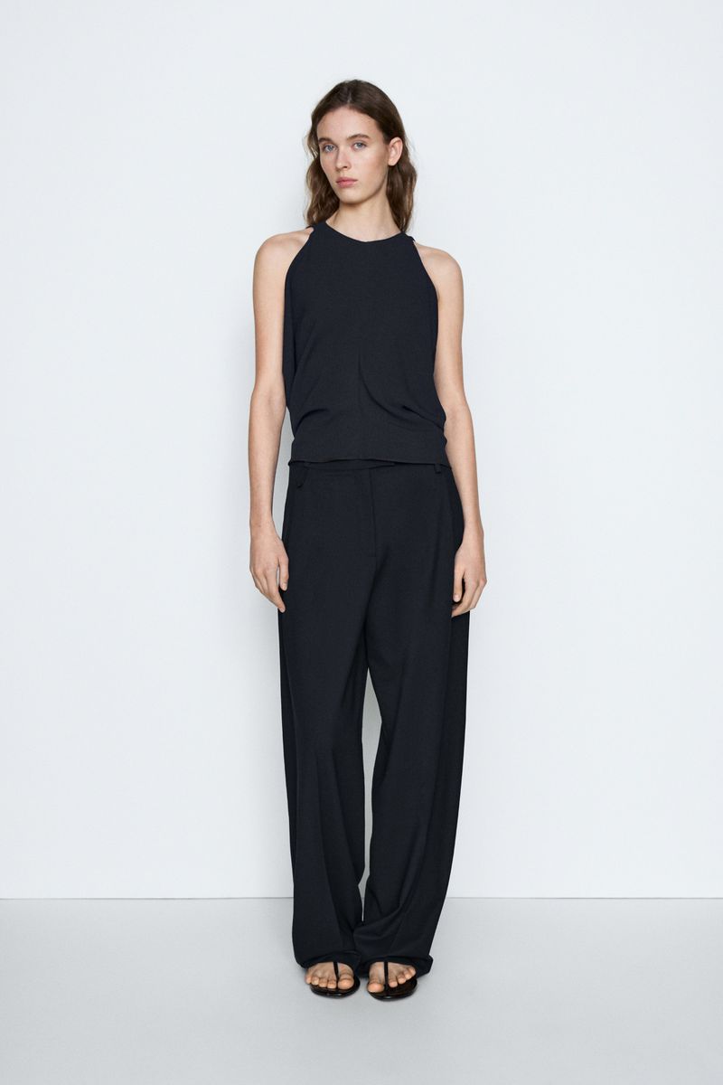 Model Liset Mitjan in a black sleeveless top and matching wide-leg trousers standing against a plain white studio background.