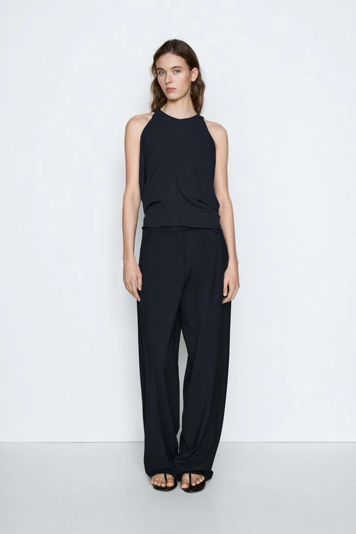 Model Liset Mitjan in a black sleeveless top and matching wide-leg trousers standing against a plain white studio background.