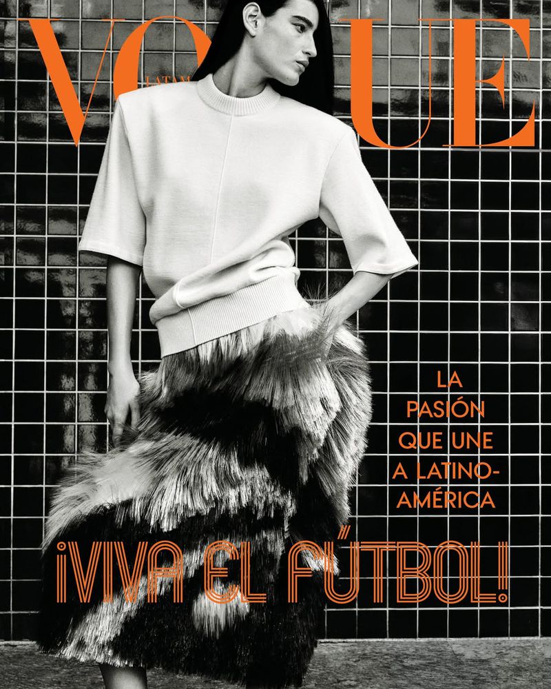 Model Luiza Perote in a white short-sleeve top and textured feather skirt against a dark tiled wall on the Vogue Latin America cover.