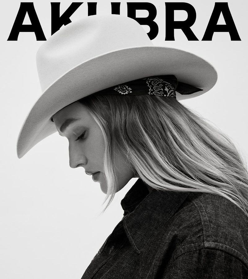 A woman wearing a white cowboy hat and denim jacket poses in a studio setting with soft lighting, showcasing fashion and beauty.