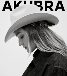 Monochrome portrait of a woman wearing a light felt cowboy hat with a patterned band and a dark shirt against a plain white background.