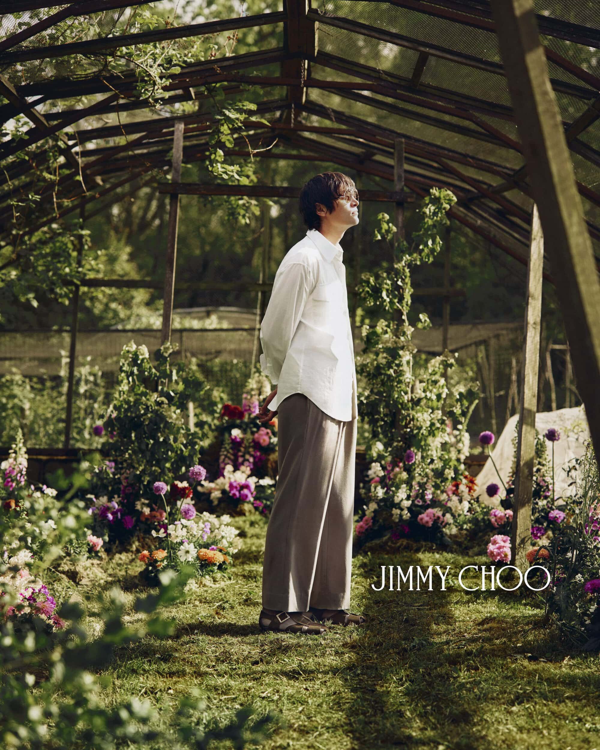 Model Alfie Nickerson in a white shirt and wide-leg trousers stands in a sunlit greenhouse for Jimmy Choo Men's Summer 2026 campaign.