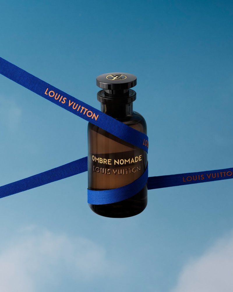 Louis Vuitton Ombre Nomade perfume bottle against a light blue sky, wrapped with a blue ribbon featuring the Louis Vuitton logo.