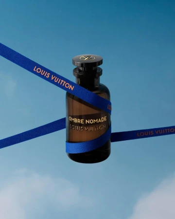 Louis Vuitton Ombre Nomade perfume bottle against a light blue sky, wrapped with a blue ribbon featuring the Louis Vuitton logo.
