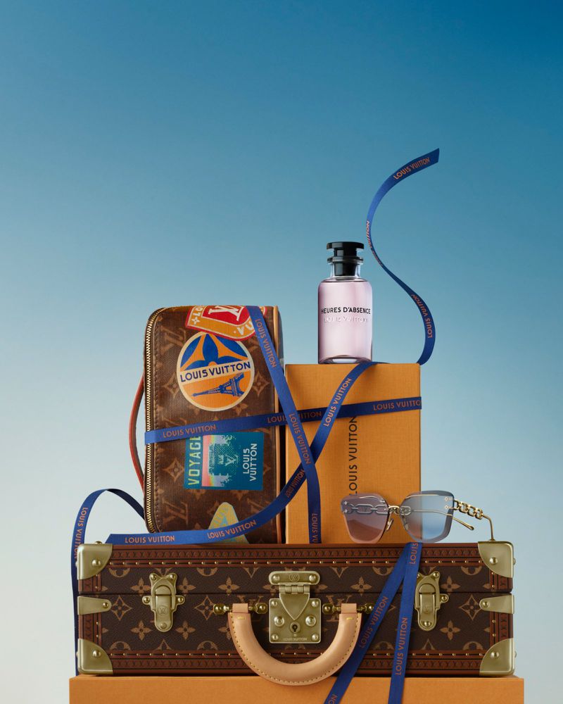 Louis Vuitton handbag, suitcase, perfume bottle, and sunglasses on orange platforms against a gradated light-blue background.