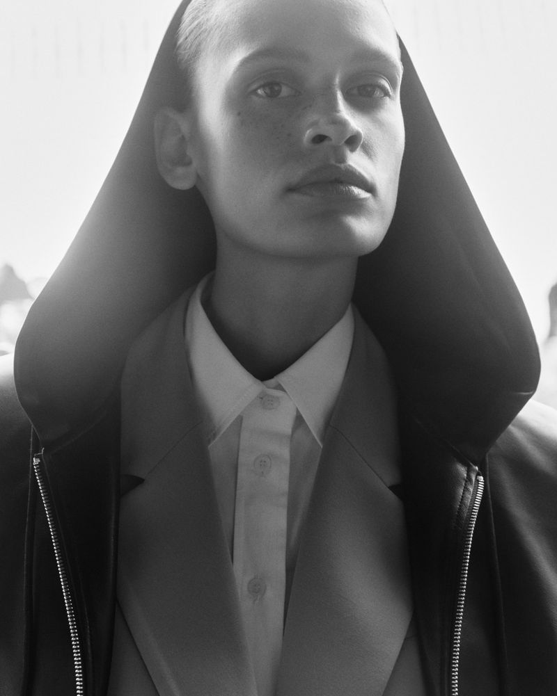 Close up portrait of a model wearing a dark hooded jacket and white collared shirt in monochrome
