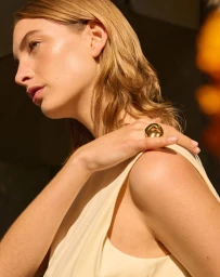 Close-up portrait of a woman wearing a cream top and a chunky gold ring, captured in warm sunlight.