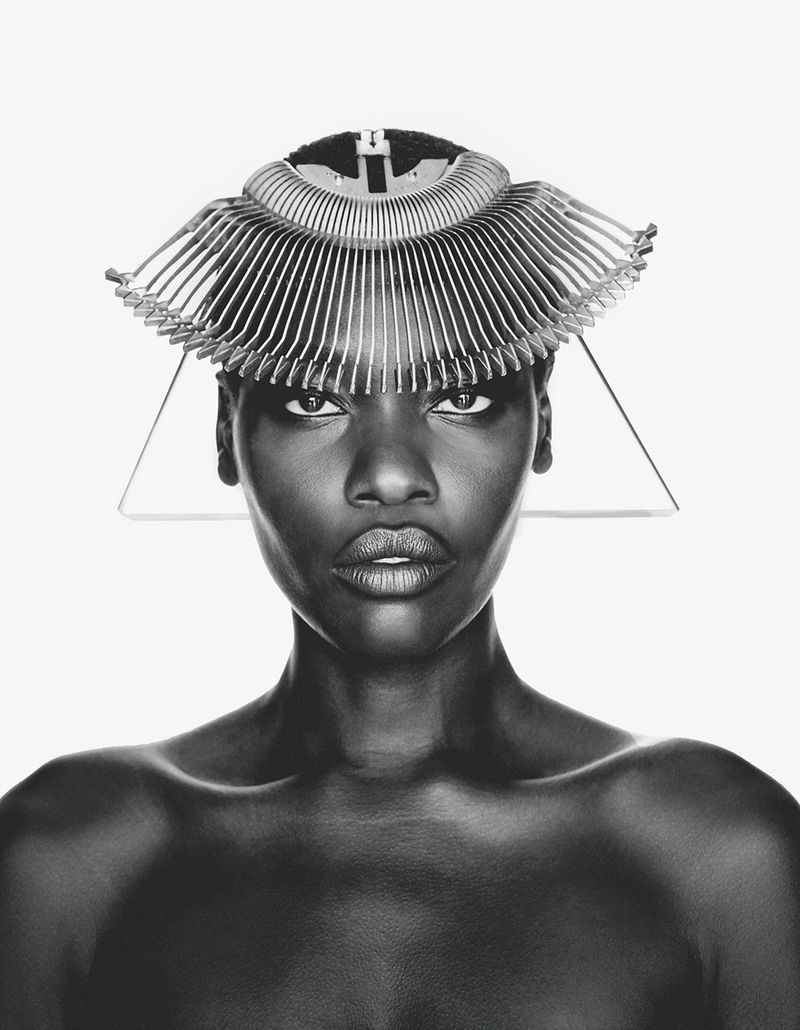 Black and white portrait of model Awar Odhiang wearing a fan-like sculptural headpiece against a pure white background.