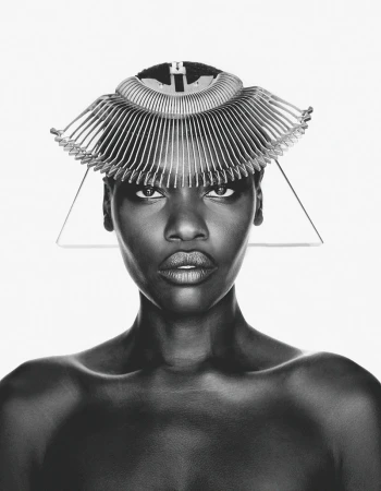 Black and white portrait of model Awar Odhiang wearing a fan-like sculptural headpiece against a pure white background.
