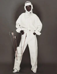 Model Awar Odhiang posing in an all-white textured outfit with a protective helmet and arrows tucked into a leg pad.