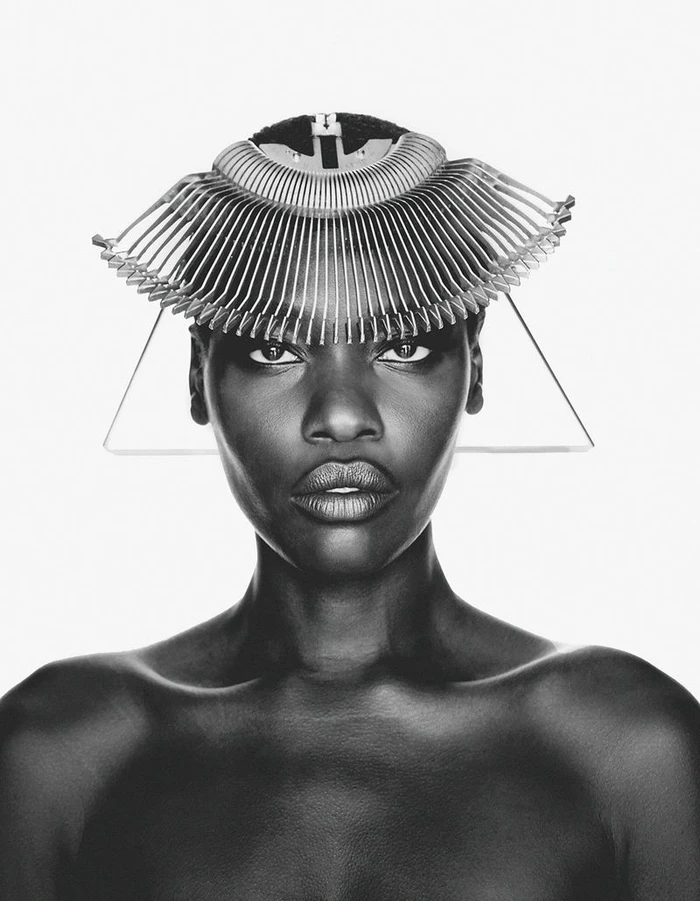 Black and white portrait of model Awar Odhiang wearing a fan-like sculptural headpiece against a pure white background.