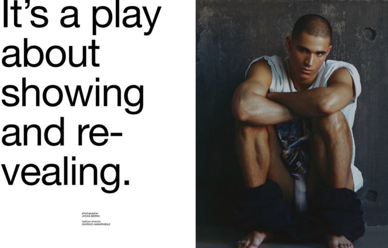 Model Melvyn Reiningi sitting with arms crossed against a dark textured concrete wall for Numero Homme Switzerland editorial