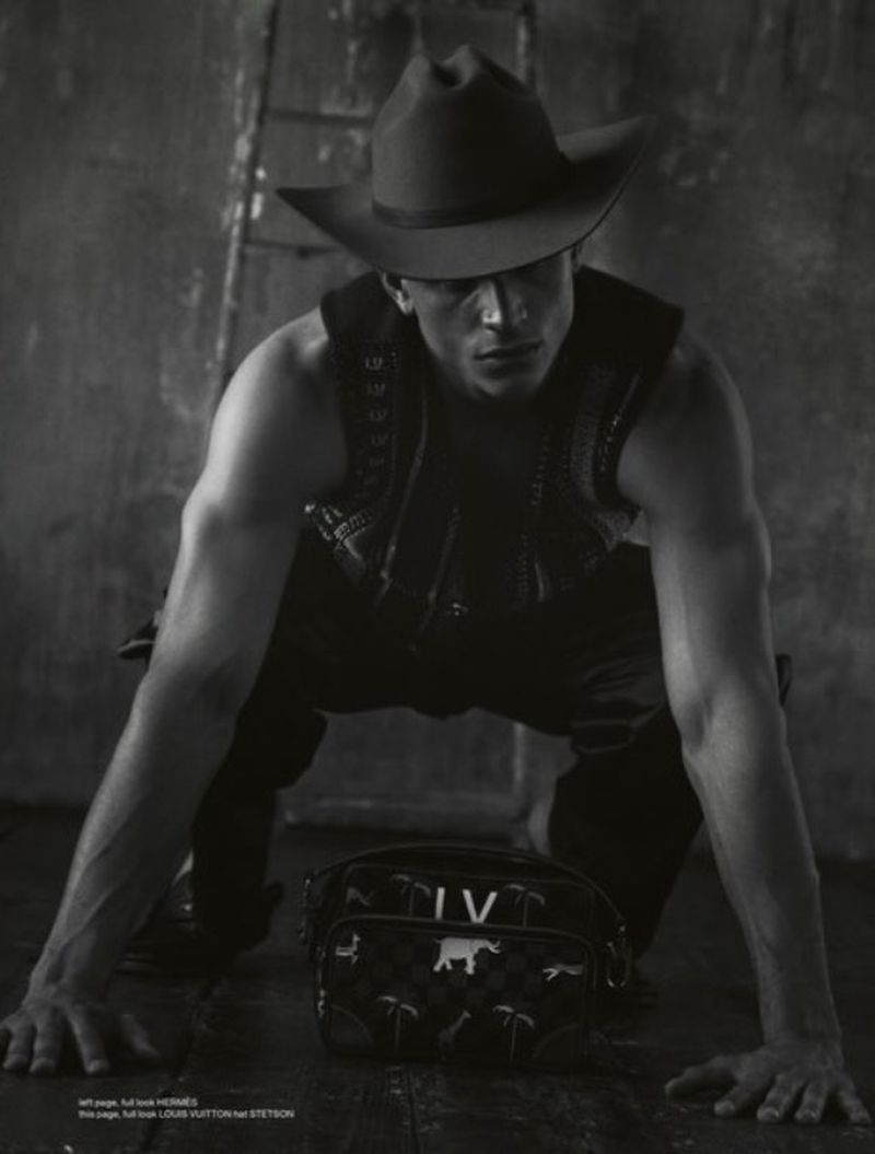 Black and white photo of model Melvyn Reiningi crouching in a cowboy hat and patterned vest with a designer bag on the floor.